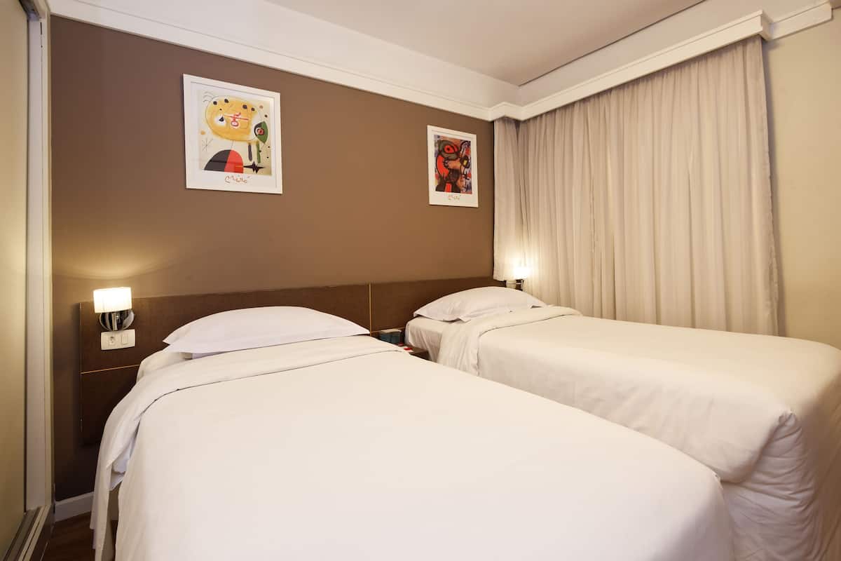 A hotel room with two beds, a brown wall, and two framed pictures.