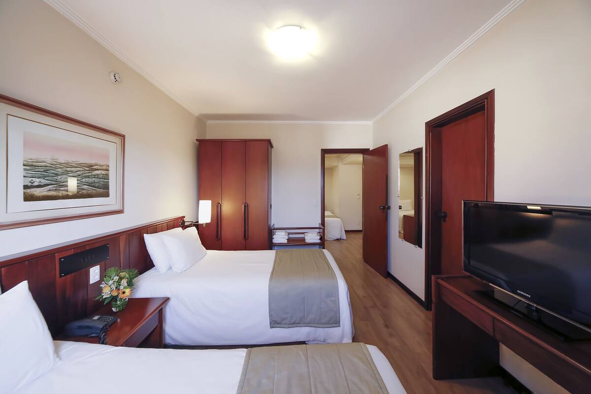 Une chambre d’hôtel avec deux lits, une télévision, un bureau et une salle de bain que l’on aperçoit à l’arrière-plan.