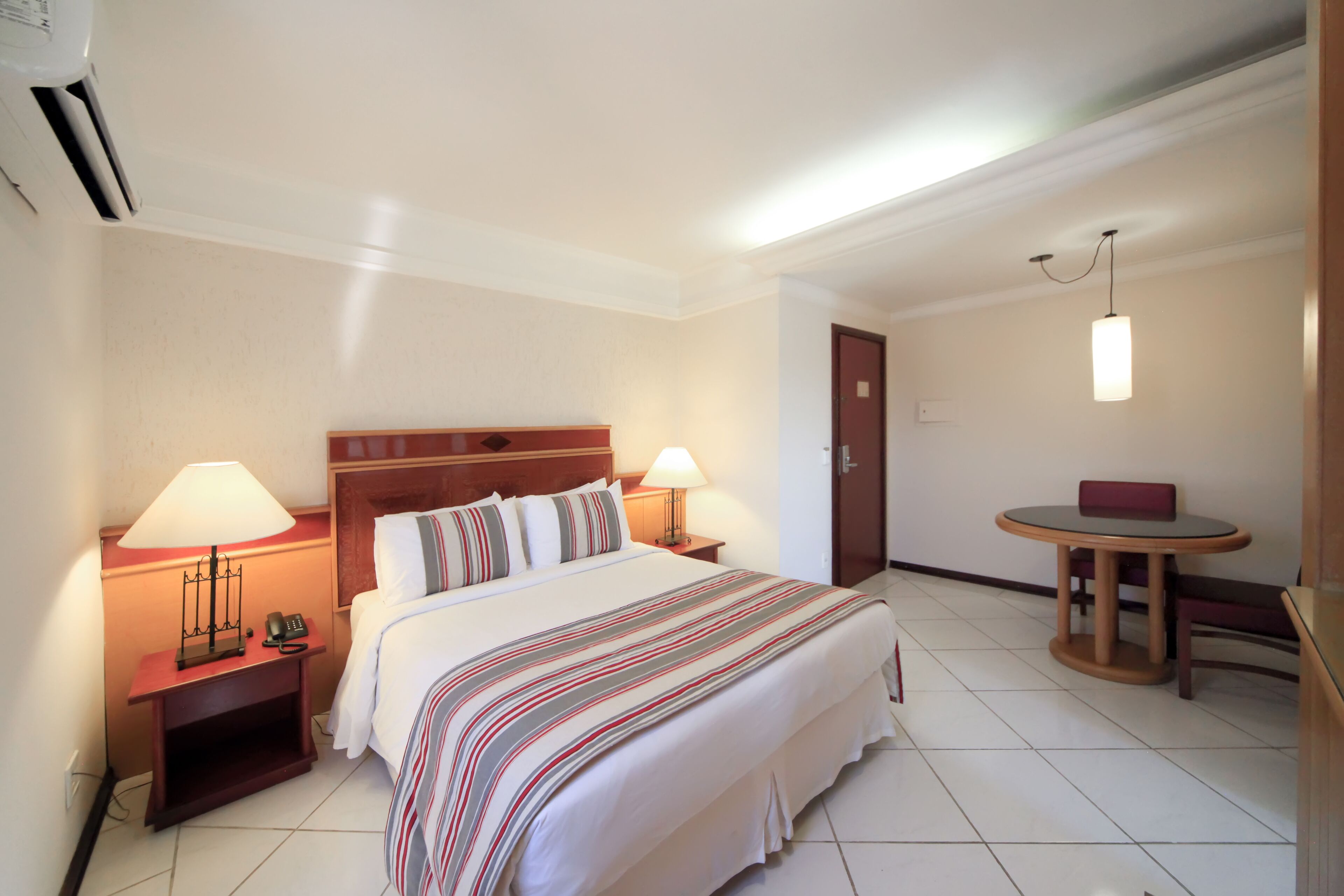 Una habitación de hotel con una cama grande, dos lámparas de noche, una mesita con una silla y una puerta.