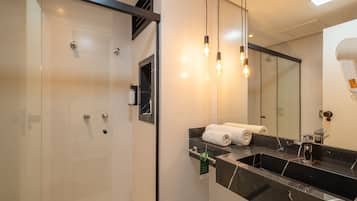 A modern bathroom with a glass shower enclosure, a black marble sink, and a large mirror.