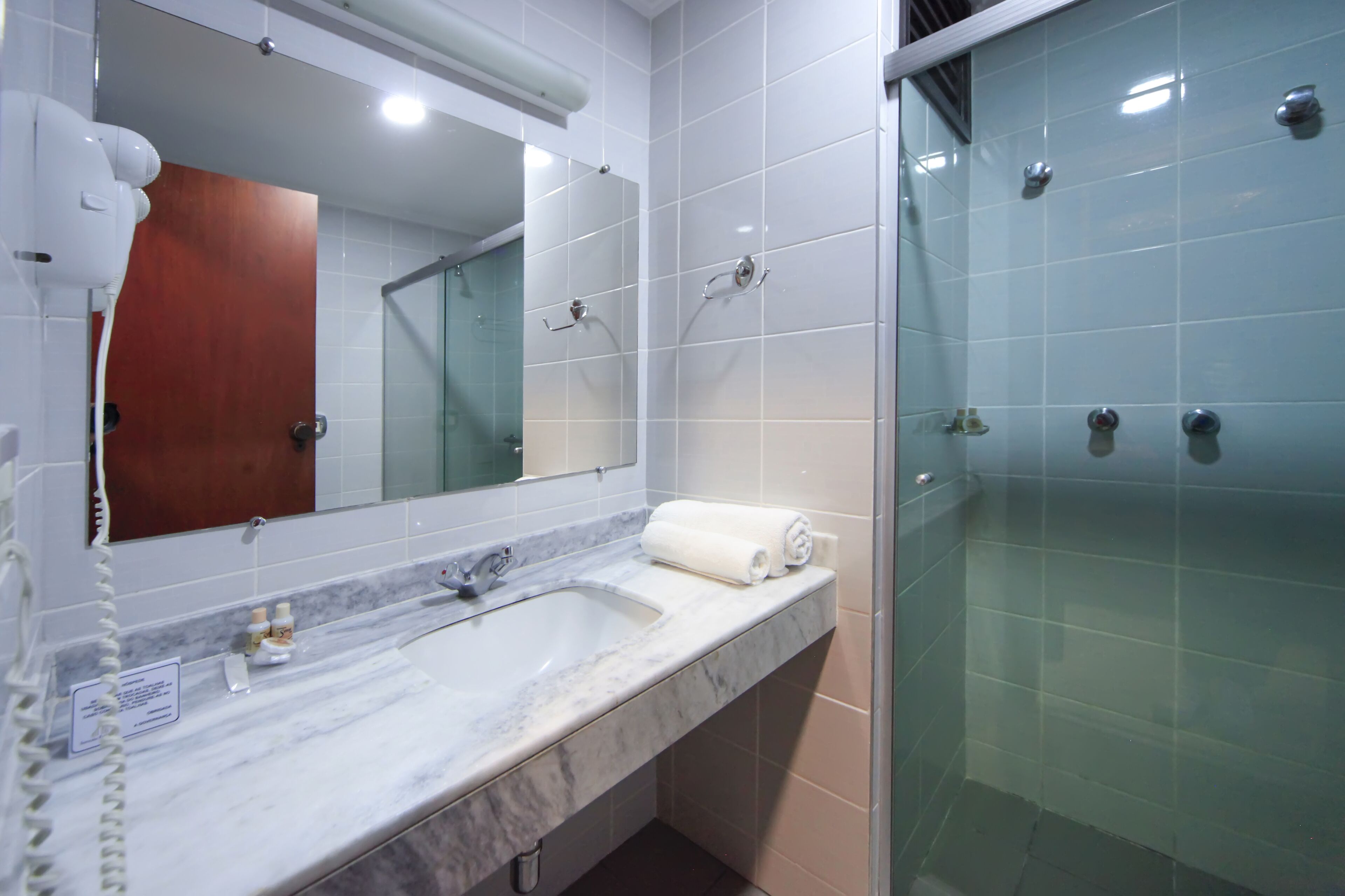 A bathroom with a marble sink, a mirror, a towel, and a glass-enclosed shower.