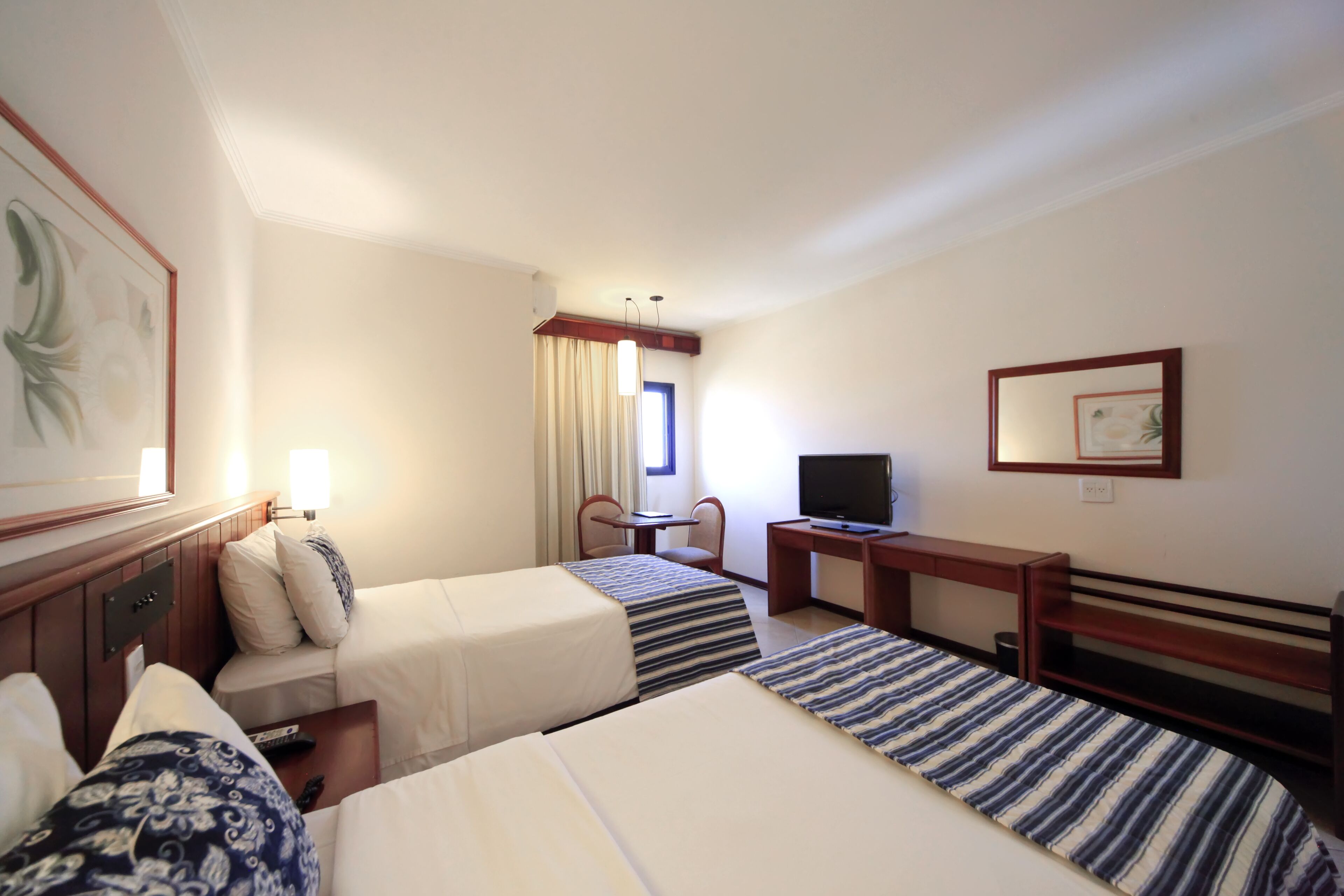 A hotel room with two single beds, a desk with a television, a chair, and a window with curtains.