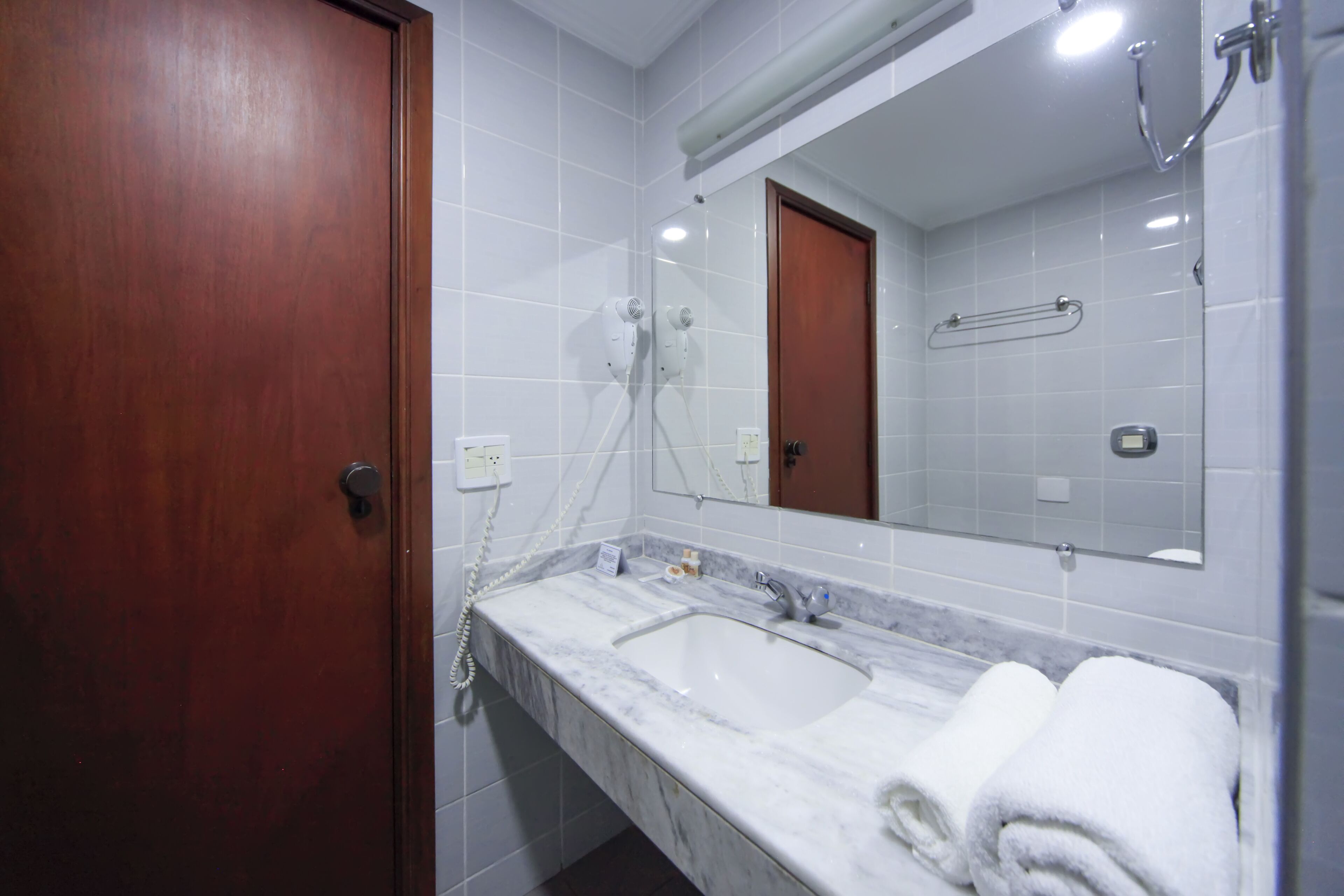 Un baño con puerta de madera, lavamanos de mármol, un espejo y un perchero para toallas.