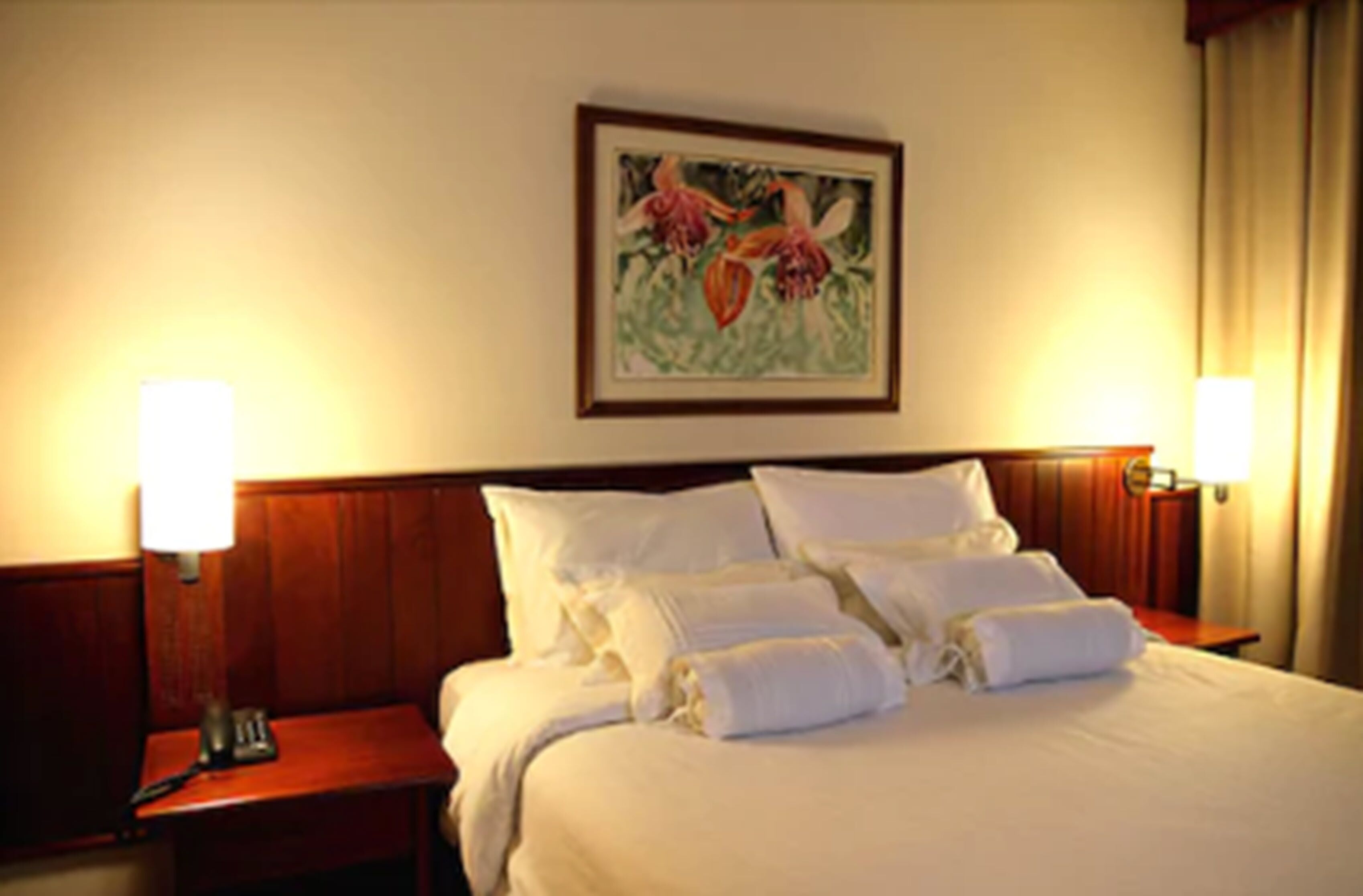 A hotel room with a neatly made bed, two bedside tables, and a framed floral artwork on the wall.