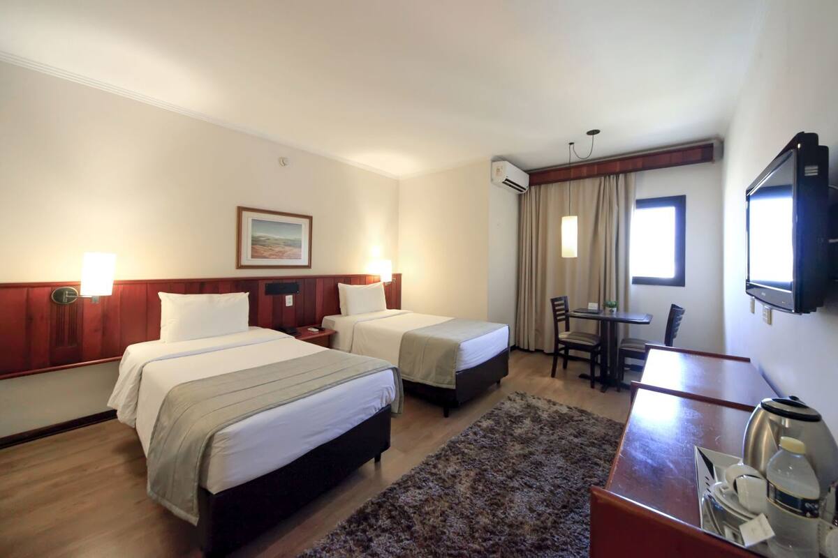 Une chambre d’hôtel avec deux lits, un bureau, une chaise, un téléviseur et un appareil de climatisation.