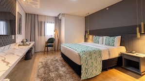 A modern hotel room with a large bed, bedside table, and a desk with a chair.