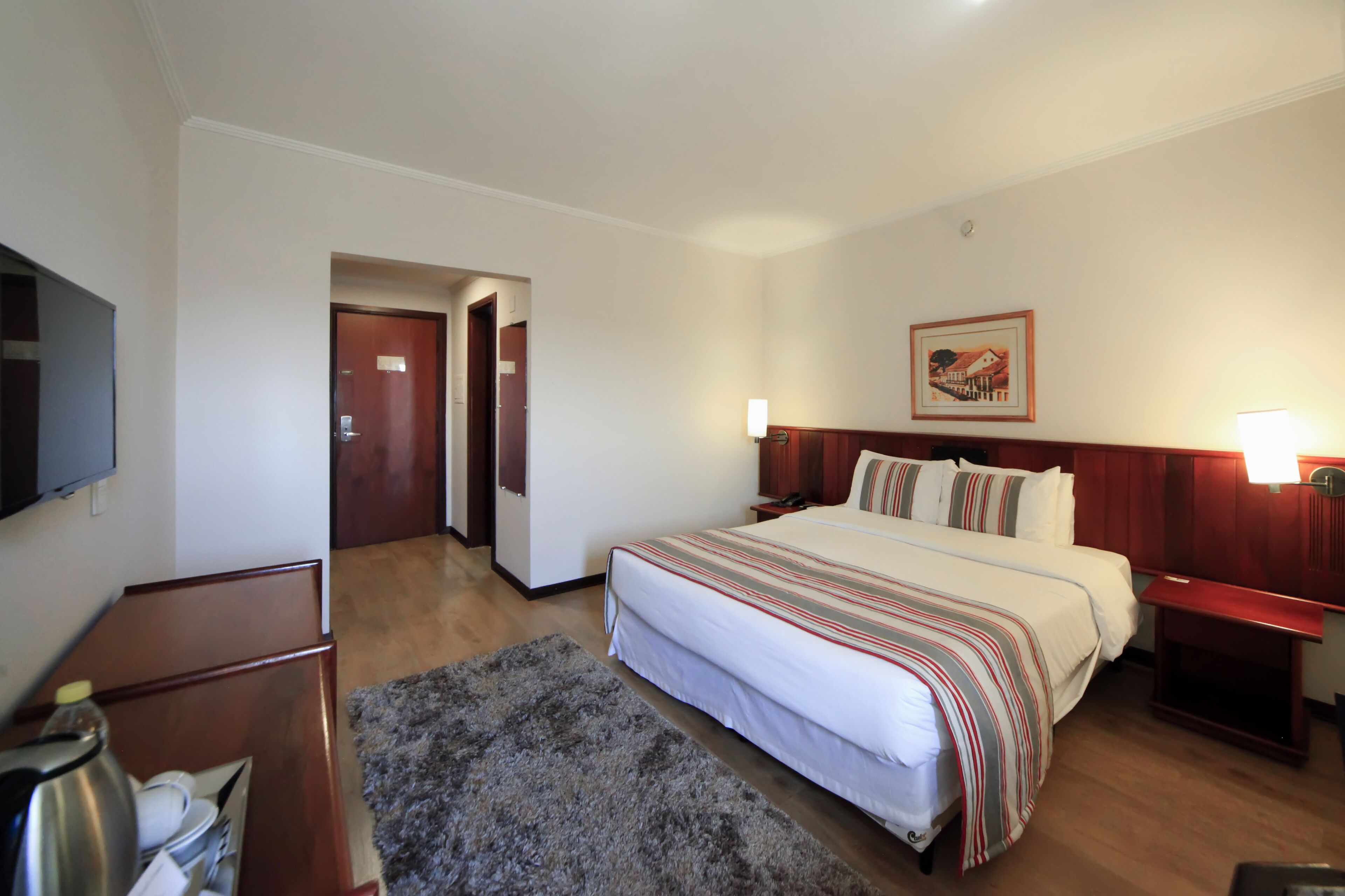 A hotel room with a large bed, a flat-screen TV, a wooden desk, and a small rug.