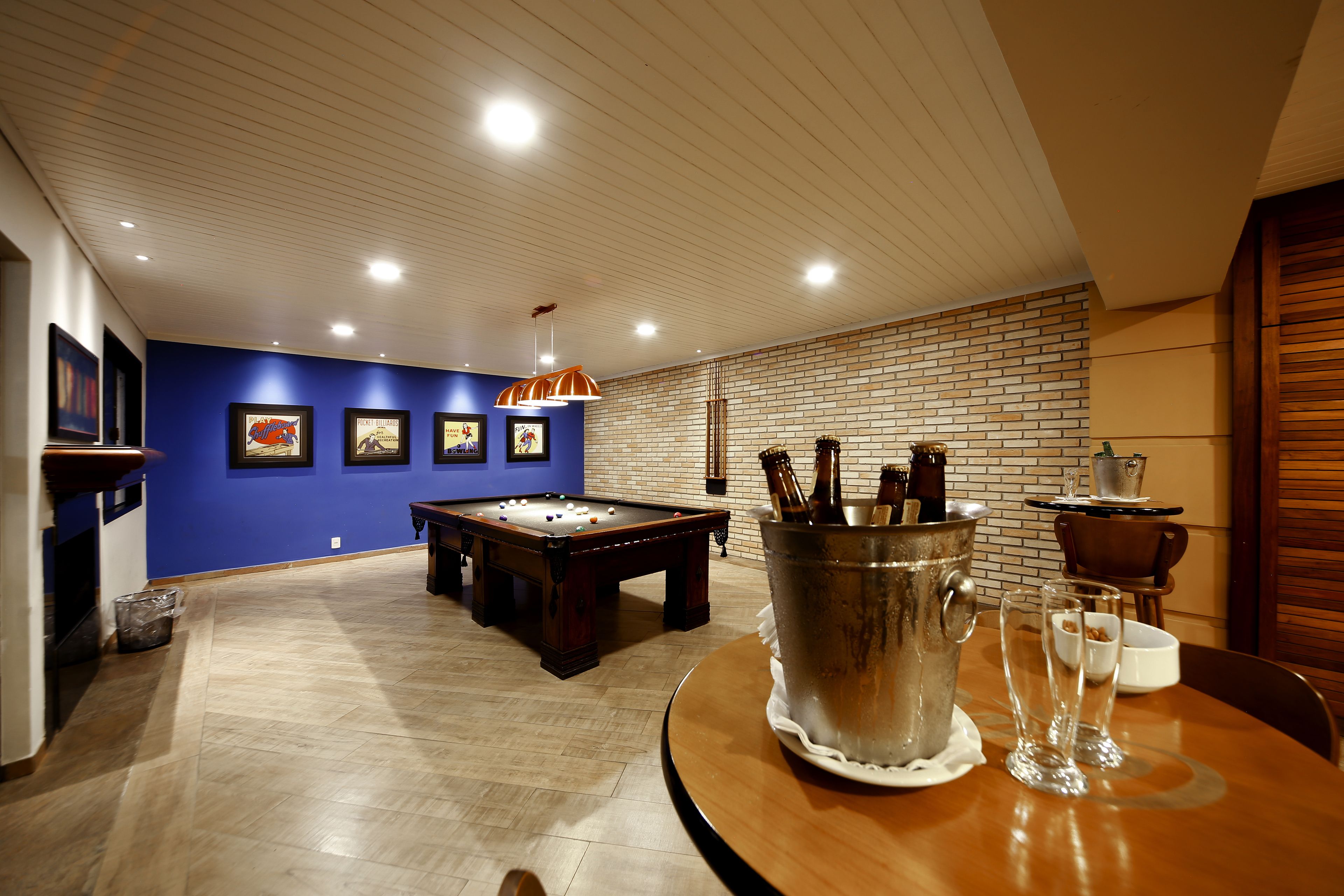Une pièce comprenant une table de billard, un coin bar avec un seau rempli de bouteilles de bière et une table à manger avec des verres.