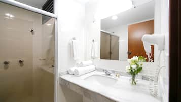 Een moderne badkamer met een glazen douchecabine, een marmeren wastafel en een haardroger op het aanrecht.
