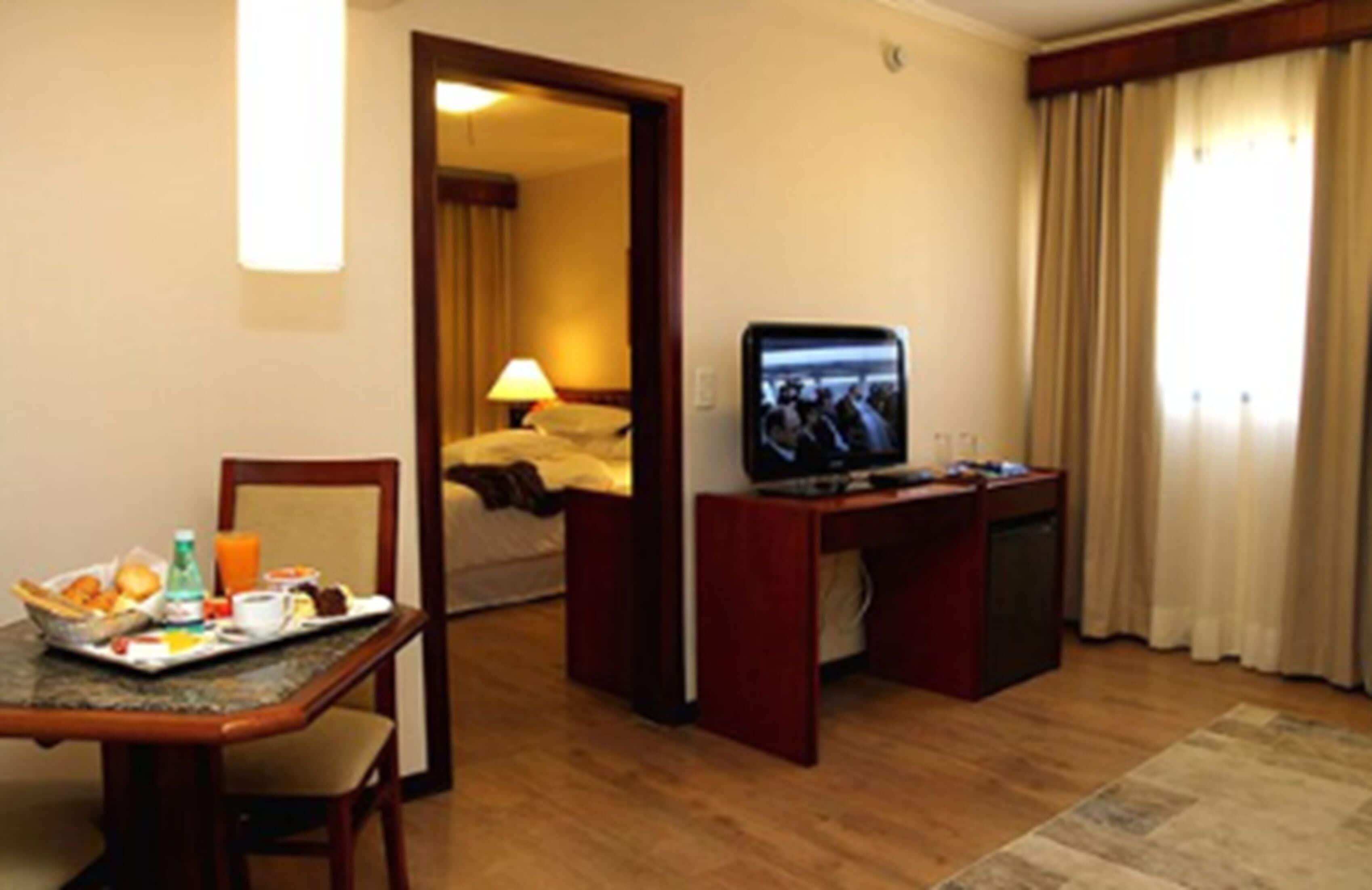 A hotel room with a dining area, a television, and a bed.