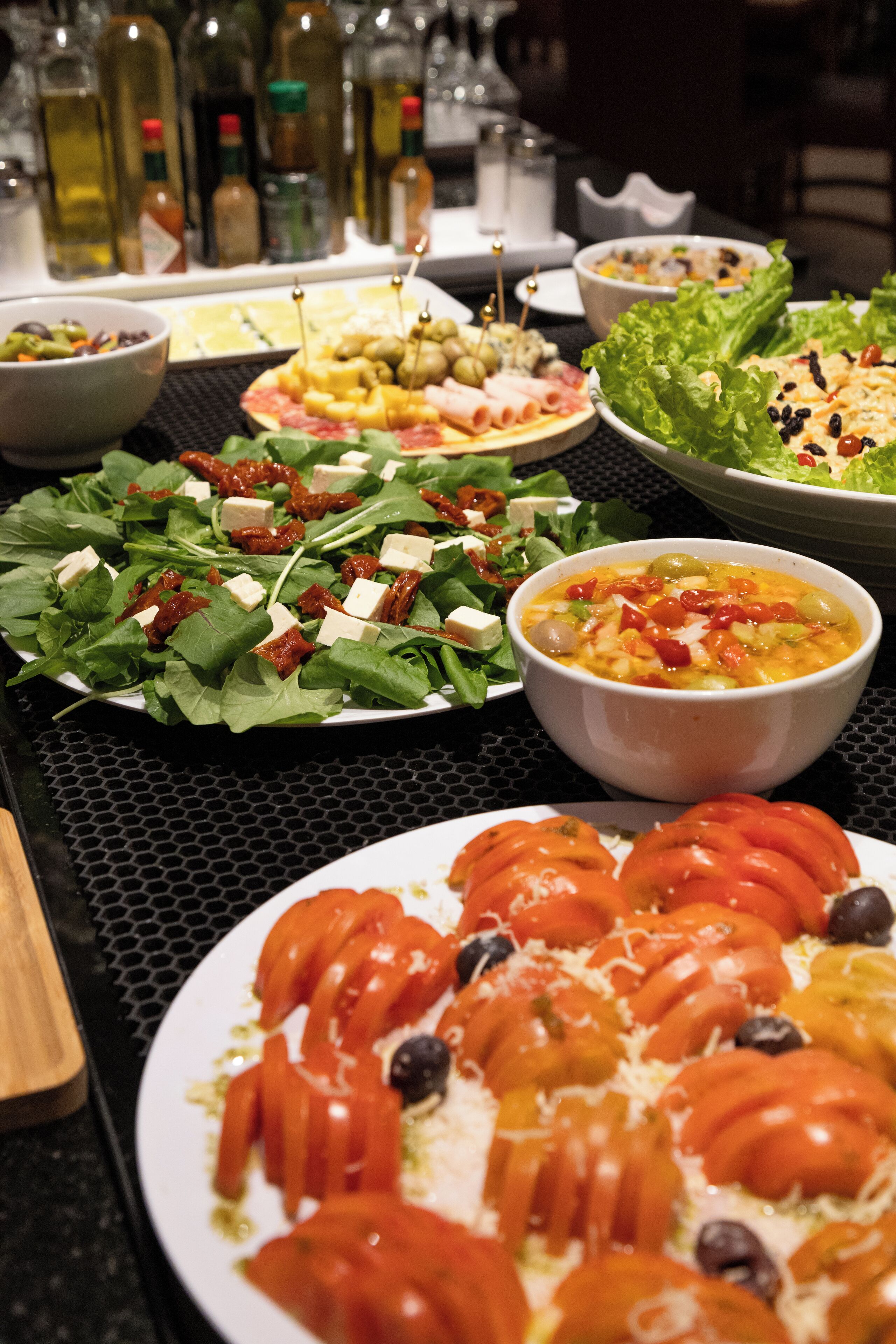 A variety of dishes on a table, including salads, a bowl of soup, and plates with sliced tomatoes and olives.
