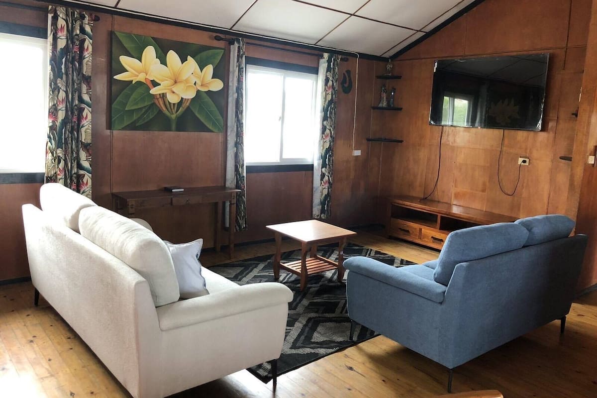 Ein Wohnzimmer mit einem weißen Sofa, einem blauen Sessel, einem kleinen Tisch und einem an der Wand befestigten Fernseher.