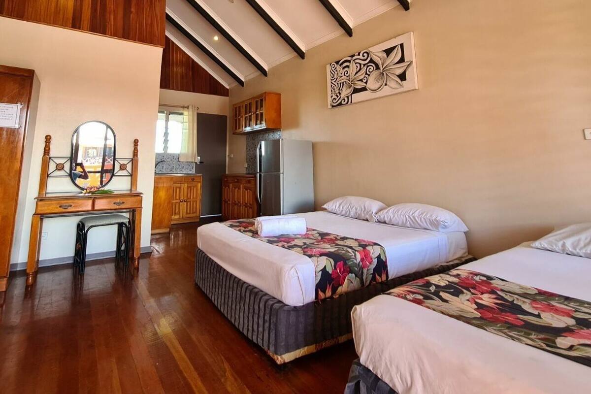 Ein Hotelzimmer mit zwei Betten, einem Holztisch, einem Spiegel und einer Küchenzeile.