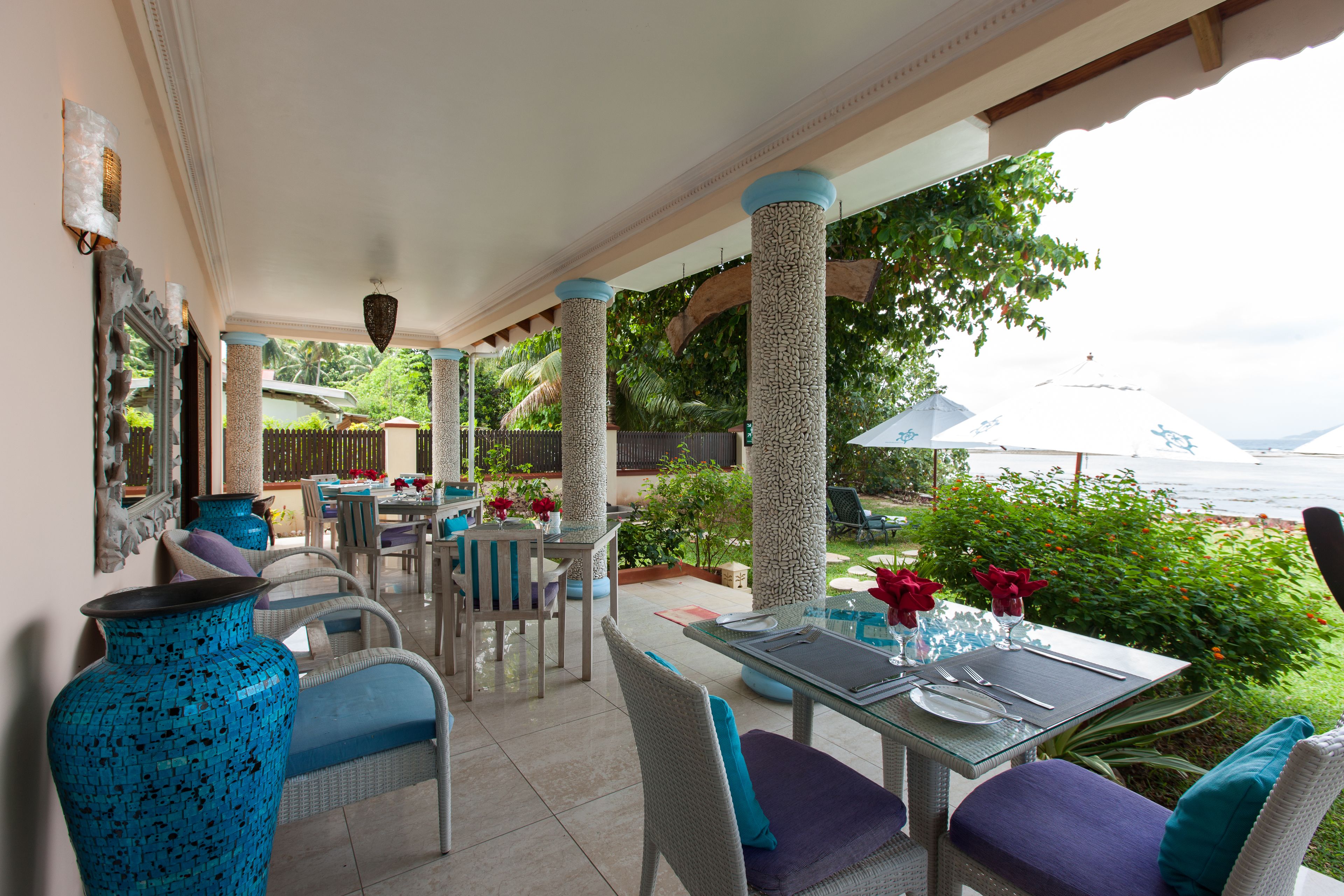 A covered outdoor dining area with wicker furniture, a glass table, and a view of the sea.