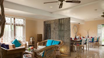 A spacious living area with wicker furniture, a dining table, and a decorative wall panel.