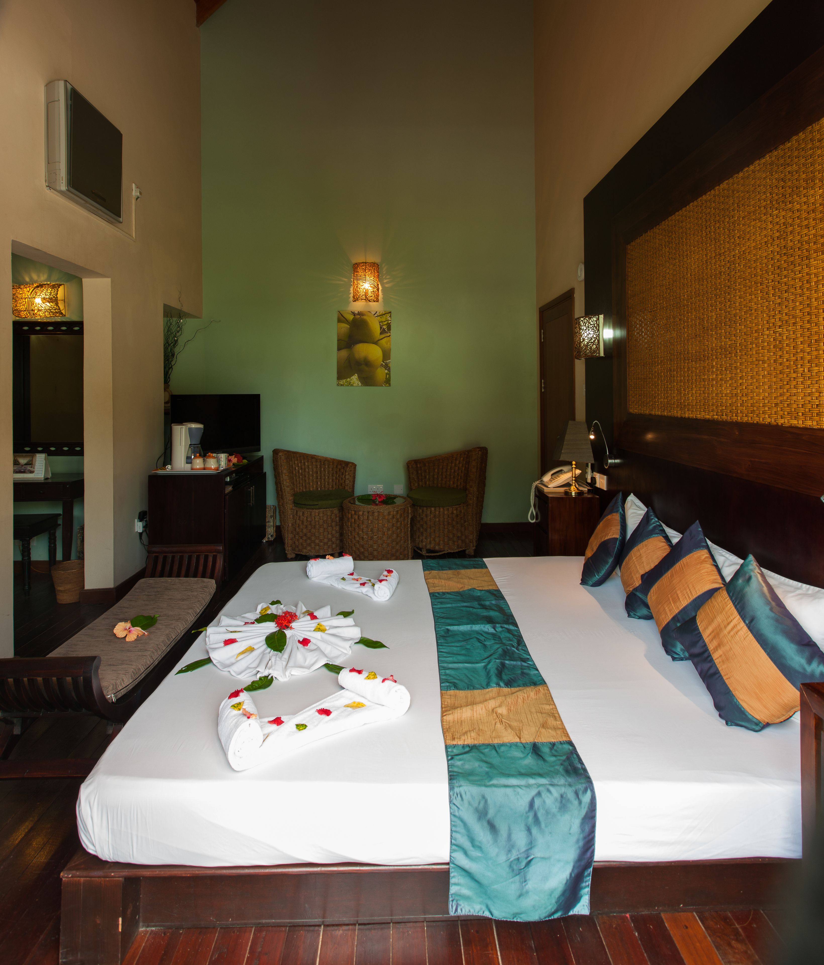 A hotel room with a large bed, two wicker chairs, a small table, and a desk with a computer.
