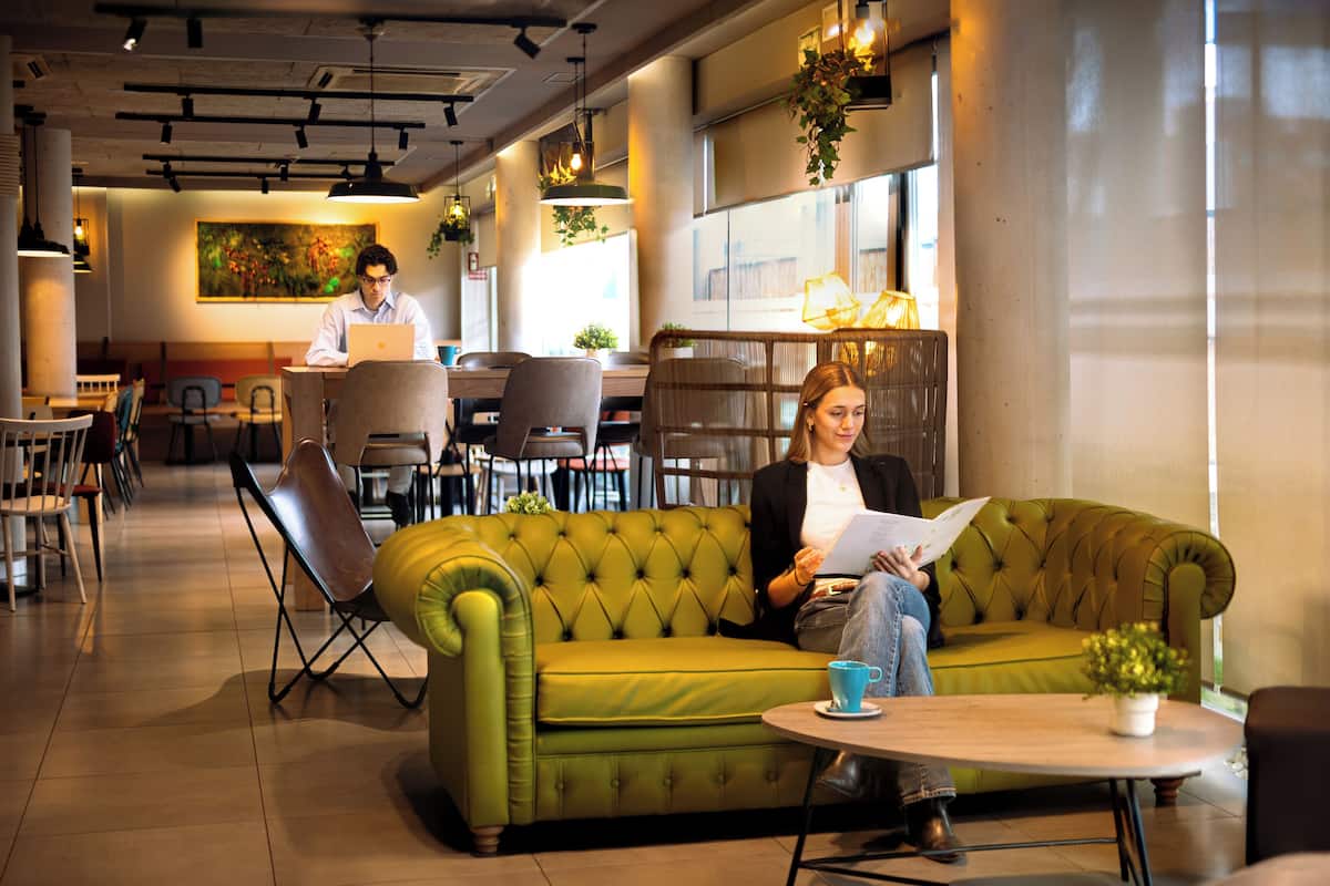 Un espace détente moderne avec un canapé vert, une table ronde et un ordinateur portable posé sur un bureau.