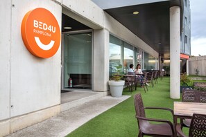 A modern building with a sign reading "BED4U PAMPLONA" and an outdoor seating area with tables and chairs. - Hotel Bed4u Pamplona (Galar)