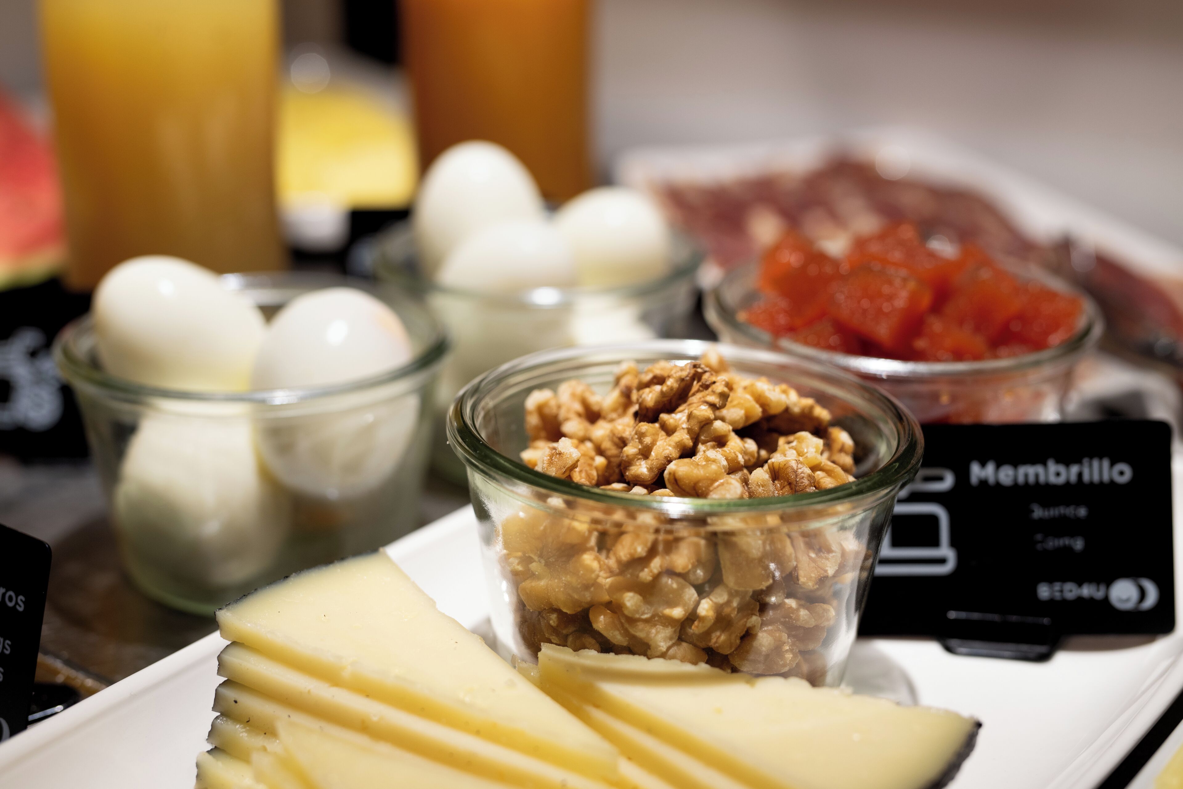 A breakfast buffet with various food items including cheese, eggs, walnuts, and a dish labeled 'Membrillo'.