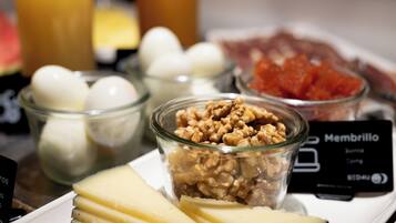 A breakfast buffet with various food items including cheese, eggs, walnuts, and a dish labeled 'Membrillo'.