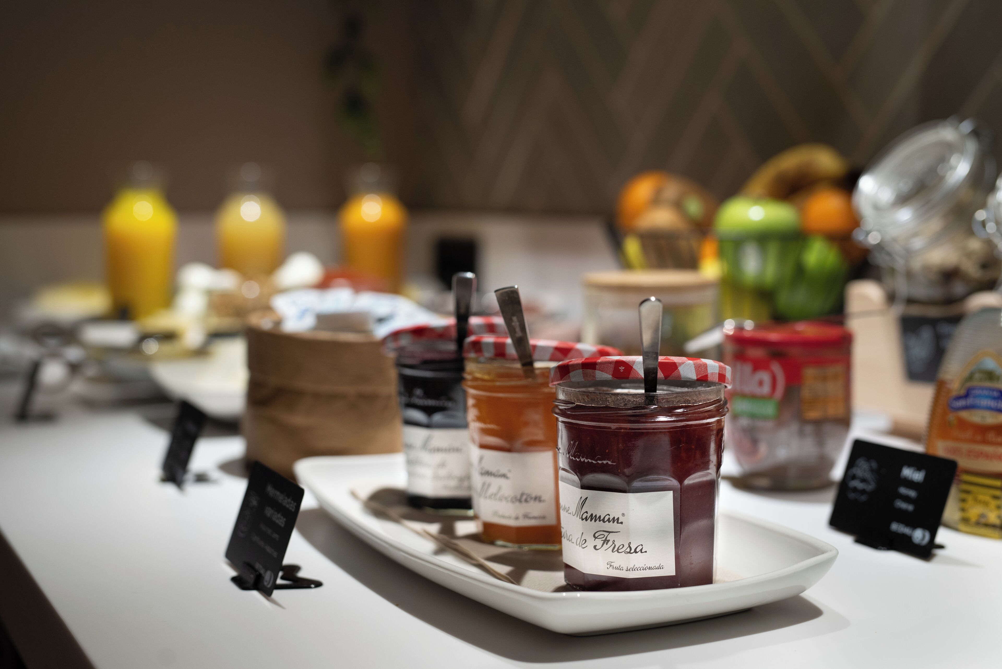 A breakfast buffet with various jams, fruits, and beverages.