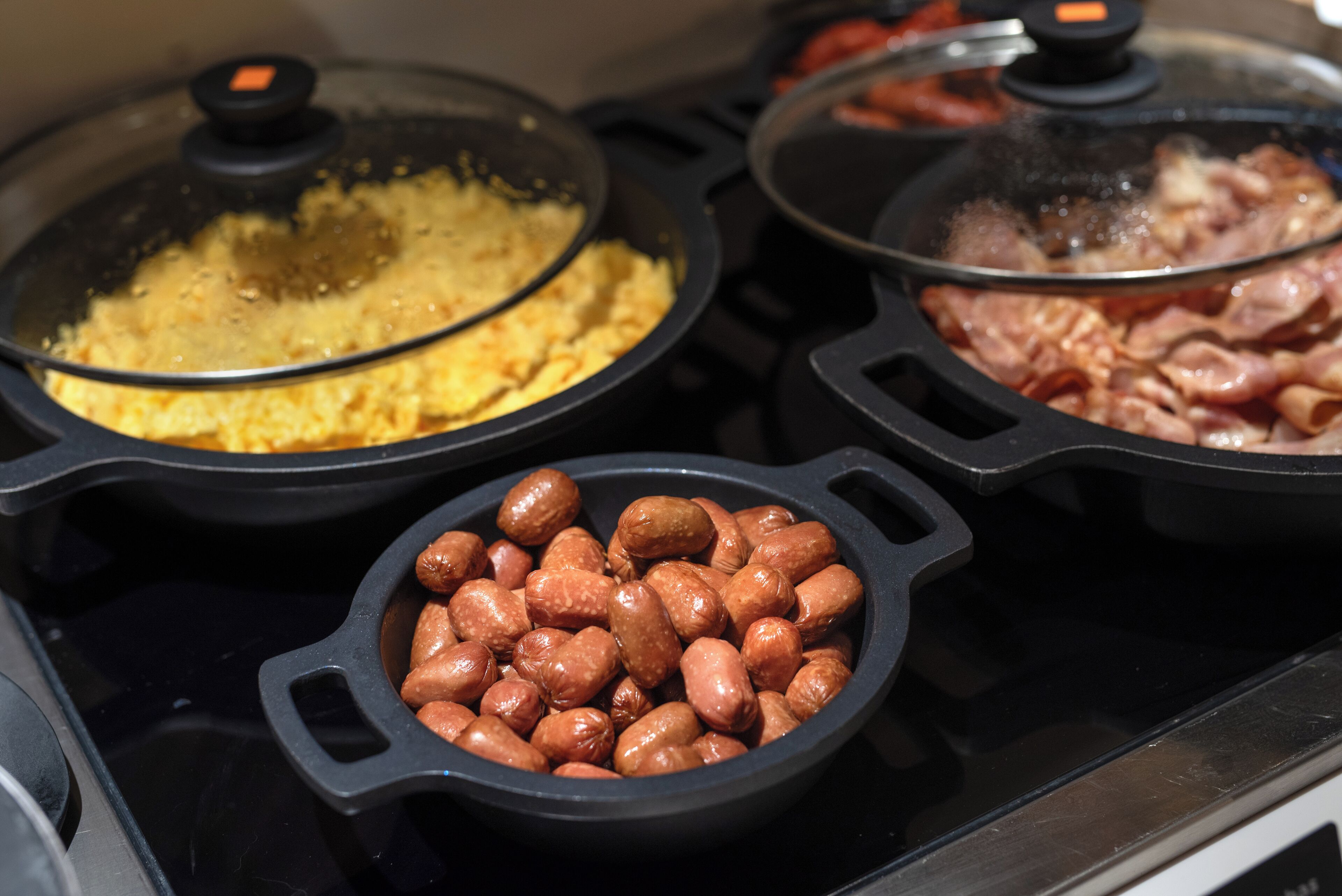Una cuina amb tres paelles de vidre, cadascuna amb aliments diferents.