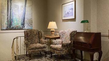 A room with a zebra-patterned carpet, two floral armchairs, a wooden sideboard, a table with a lamp, and a framed picture on the wall.