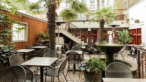 Un espace café en plein air avec des tables et des chaises, une fontaine et des plantes.