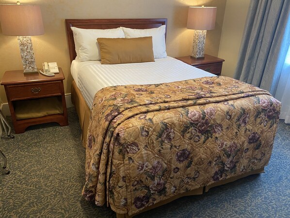Una habitación de hotel con una cama grande, dos mesitas de noche con lámparas, un teléfono y una colcha estampada con motivos florales.