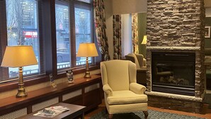 Une pièce chaleureuse avec une cheminée en pierre, un fauteuil confortable, un banc en bois agrémenté de lampes et une fenêtre avec des stores.