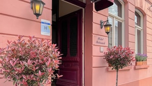 A pink building with a dark red door, a sign indicating it's a hotel, and a small window with a plant. - Botaniek (Bruges)