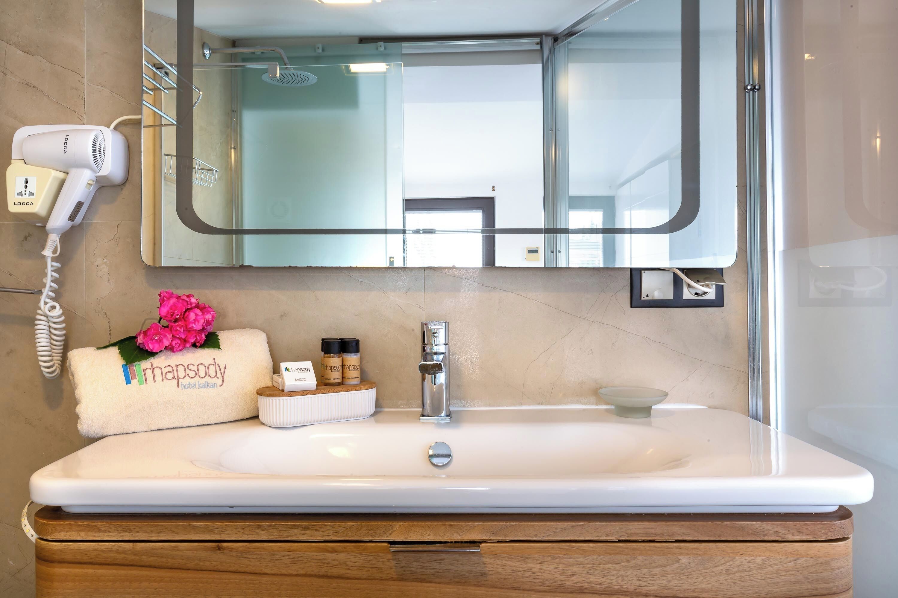 Un baño moderno con un espejo grande, un lavabo blanco y un secador de pelo en la pared.