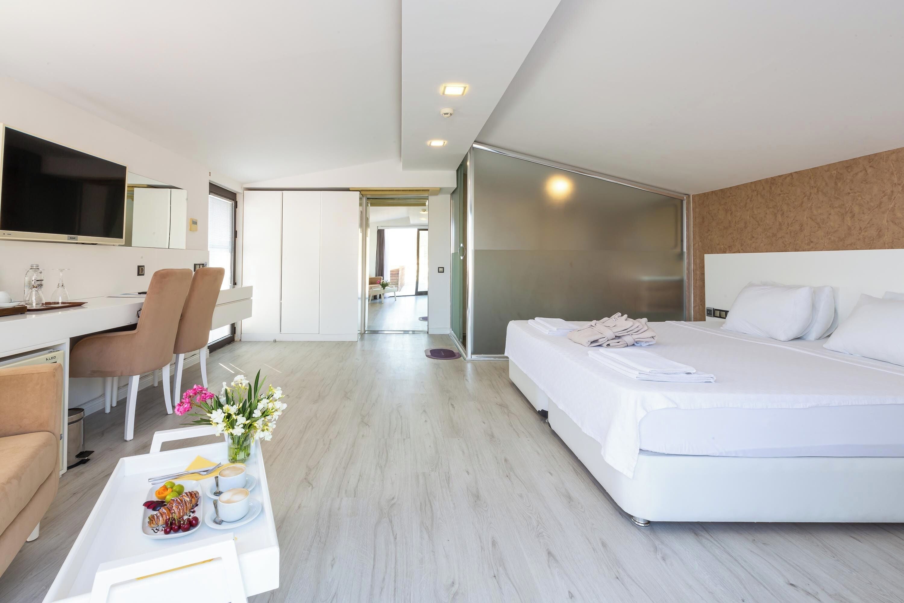 Une chambre d’hôtel moderne avec un lit, un bureau et des chaises. On trouve sur le bureau un plateau avec des fruits et une tasse de café.
