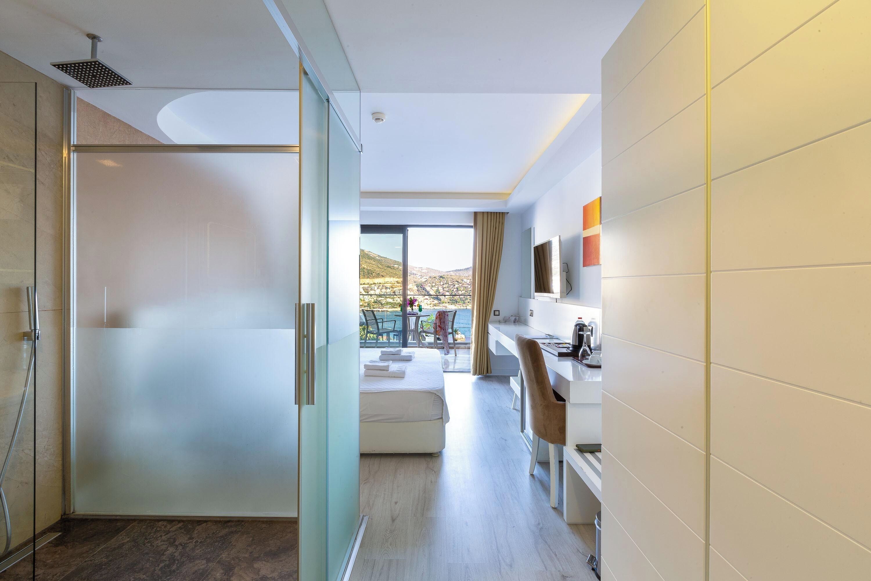 Una habitación de hotel moderna con cabina de ducha de vidrio, cama, escritorio y vistas al exterior.