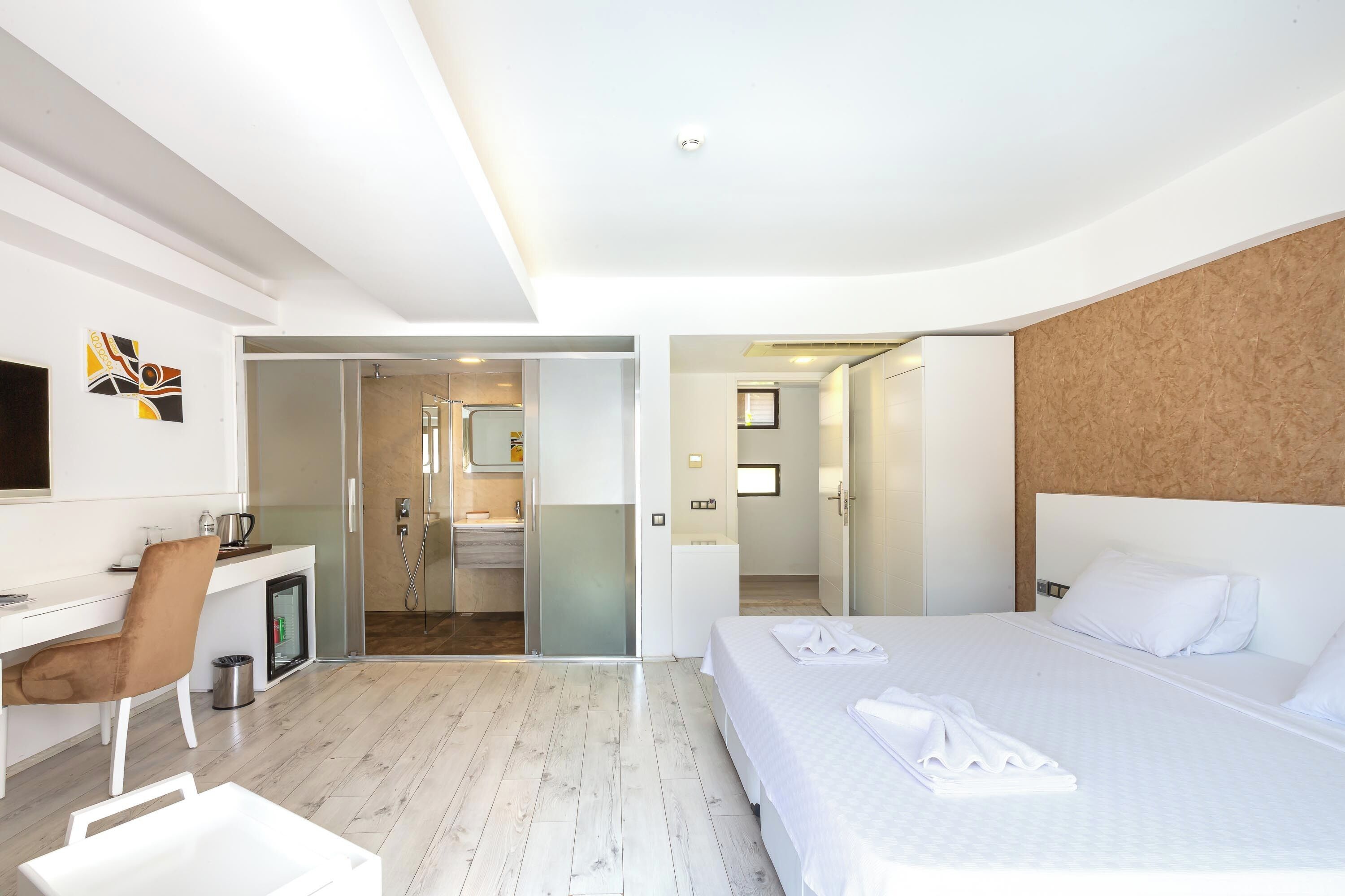 A modern hotel room with a bed, a desk, a chair, and a shower area.