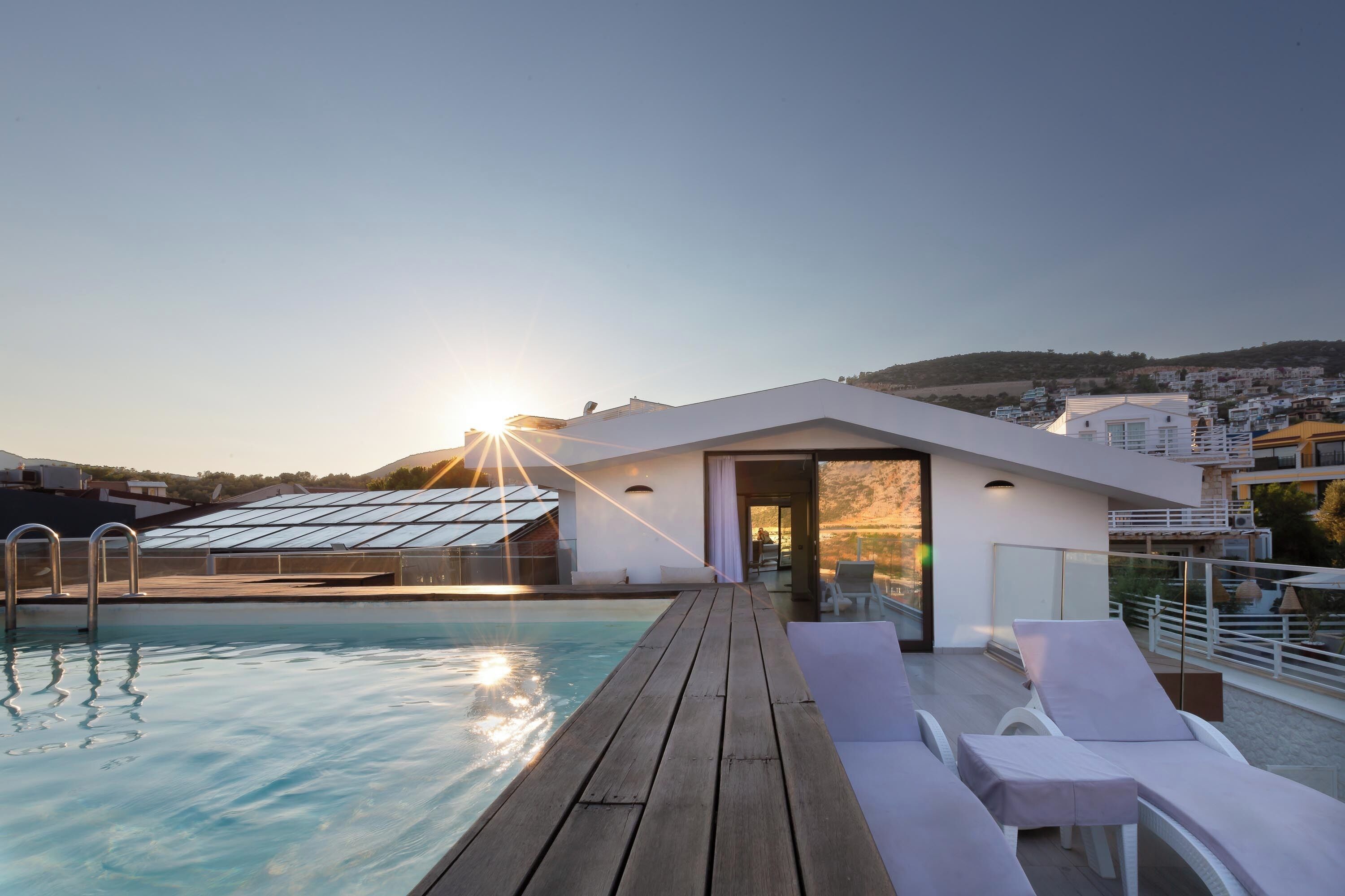 A swimming pool with a wooden deck, lounge chairs, and a glass-enclosed area.