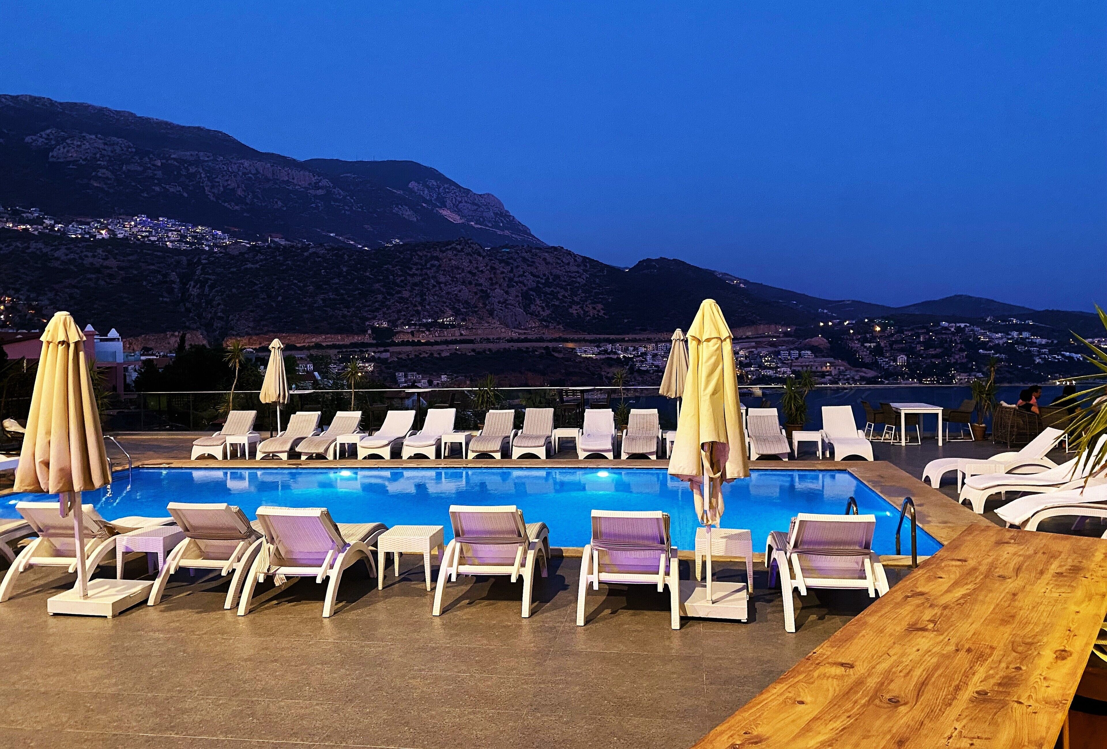Un espace aménagé au bord de la piscine, avec des chaises longues et des parasols, offrant une vue sur un paysage montagneux.
