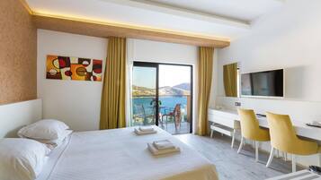 Habitación de hotel con cama, escritorio con sillas, televisor y balcón con vista al mar.