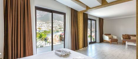 Une chambre d’hôtel avec un grand lit, un canapé et un fauteuil. Les fenêtres sont dotées de rideaux et offrent une vue sur le paysage urbain.