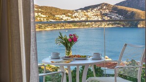 A balcony with a table set for breakfast, a vase of flowers, and a view of a coastal town.