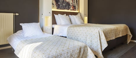 A hotel room with two beds, a large abstract painting on the wall, and a radiator.