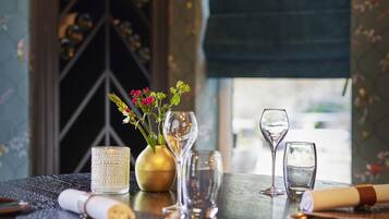Una mesa de comedor con un jarrón de flores, dos copas de vino y un mantel enrollado.
