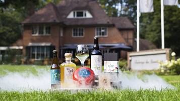A bottle of Vermouth, a wine glass, and a bottle of 1712 wine on a grassy lawn with a house in the background.
