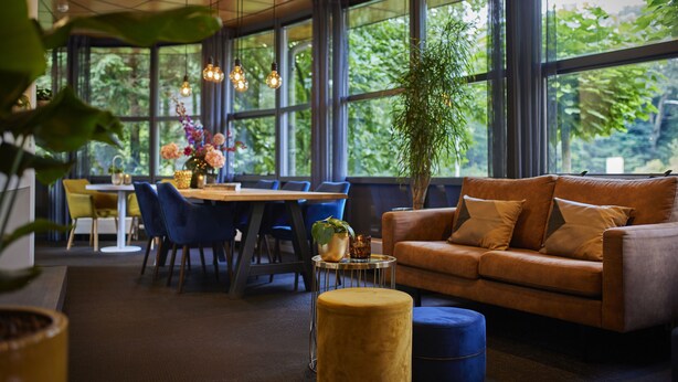 A spacious room with a large window, a sofa, a dining table with chairs, and a potted plant. - Auberge du Bonheur (Tilburg)
