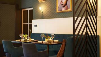 Een eethoek met een tafel gedekt voor twee personen, blauwe fauteuils en een behang met een patroon.