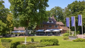 A large brick building with a garden, outdoor seating, and flags. - Auberge du Bonheur (Tilburg)
