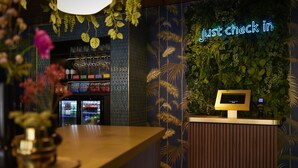 A reception desk with a digital kiosk, a neon sign, and a wall decorated with foliage. - Auberge du Bonheur (Tilburg)