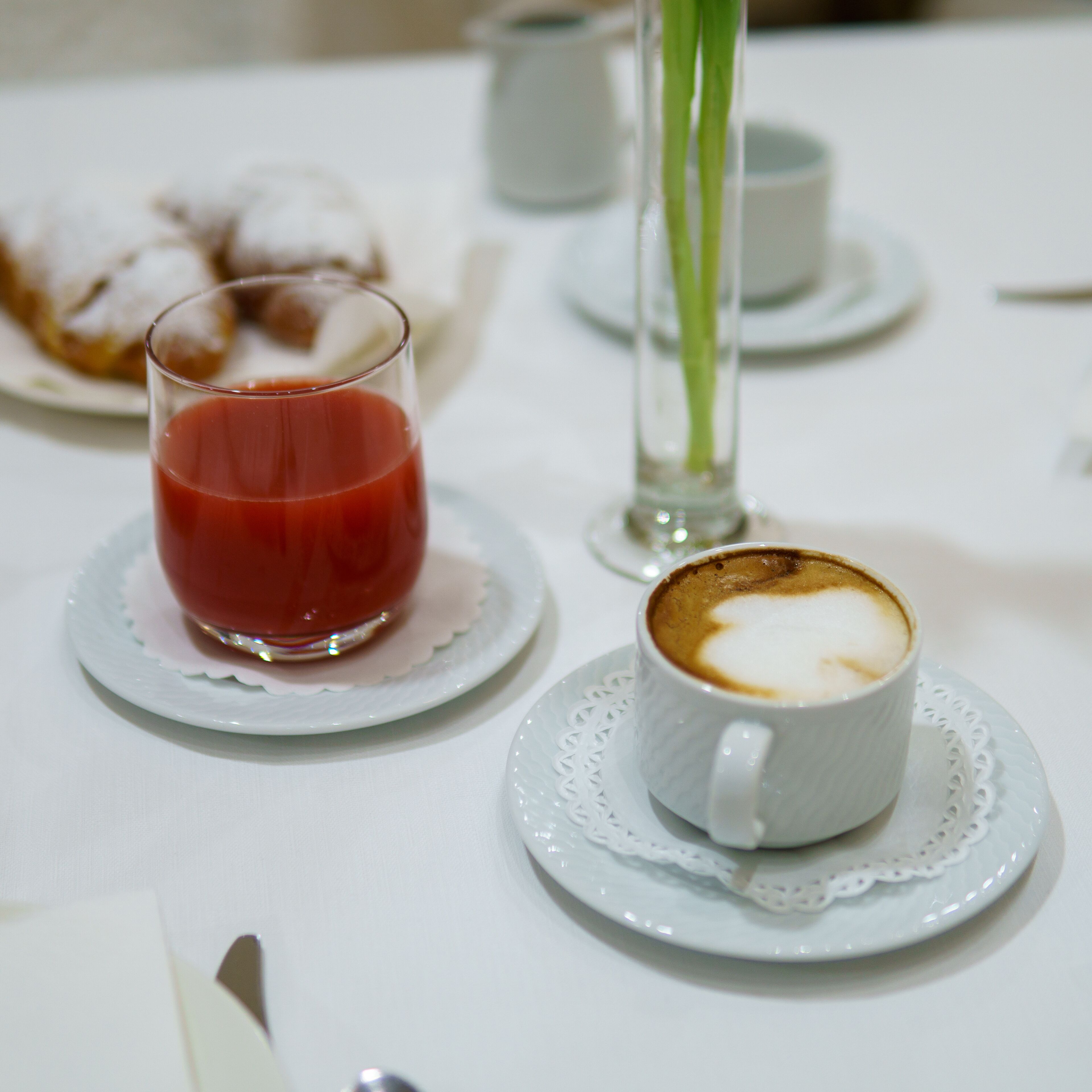 A table setting with a glass of red juice, a cup of coffee with latte art, and a plate of pastries.