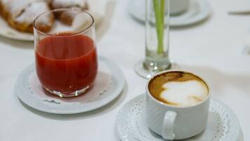 A table setting with a glass of red juice, a cup of coffee with latte art, and a plate of pastries.