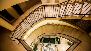 Un hotel elegante con una escalera curva, una zona de estar central y un letrero que dice 'Grand Hotel Elite'.